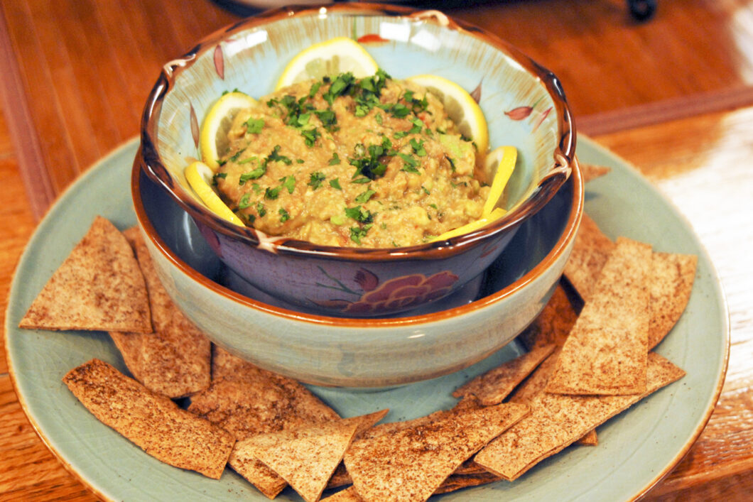 A bowl of homemade salsa on a table with a basket of tortilla chips nearby