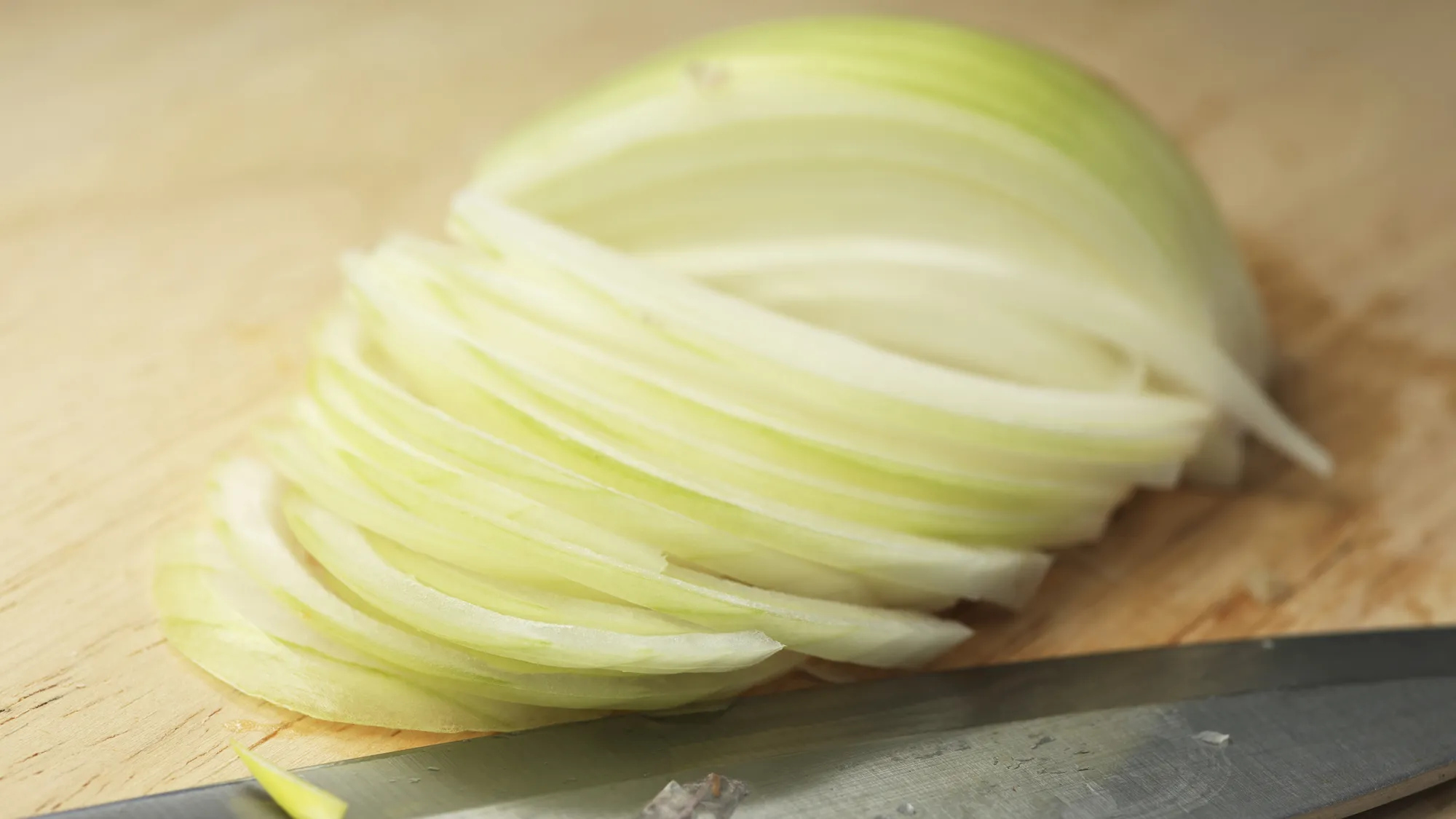 A bowl of thinly sliced yellow onions on a cutting board next to a chef's knife, ready for caramelizing