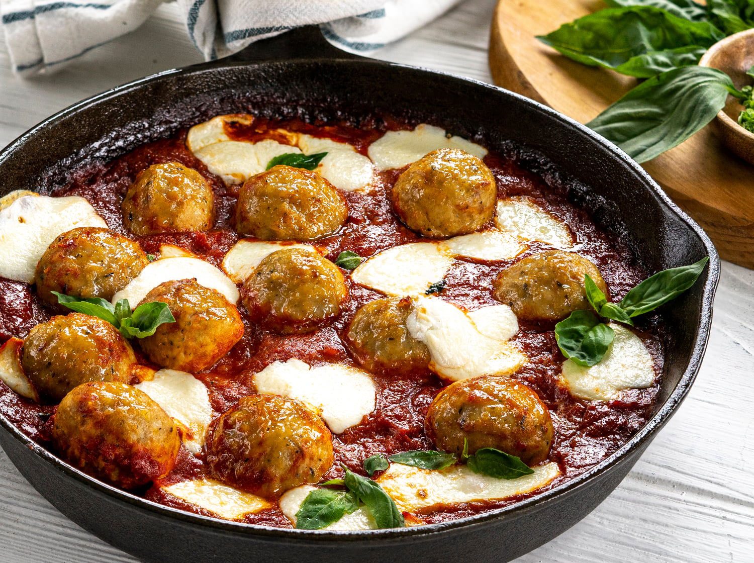 A cast-iron skillet filled with browned beef and pork meatballs simmering in marinara sauce with fresh basil scattered on top