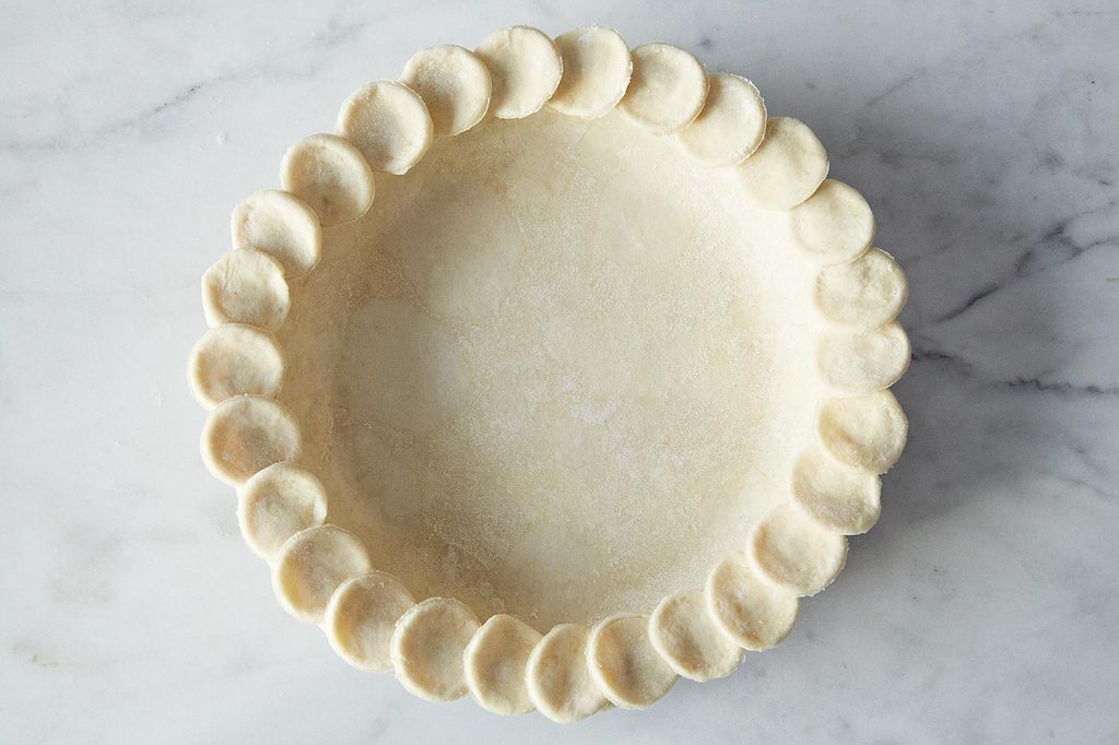 A close-up photo of a round sheet of all-butter pie dough being rolled out on a lightly floured countertop with a wooden rolling pin