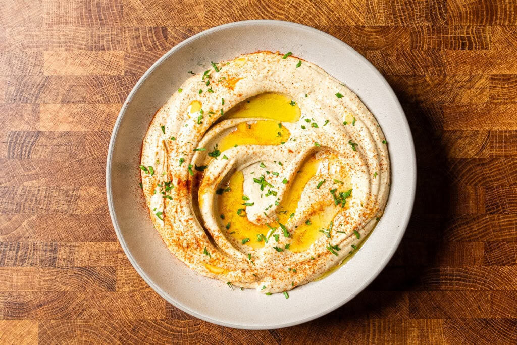 A creamy bowl of classic chickpea hummus swirled with a spoon, topped with olive oil and chickpeas, on a kitchen counter