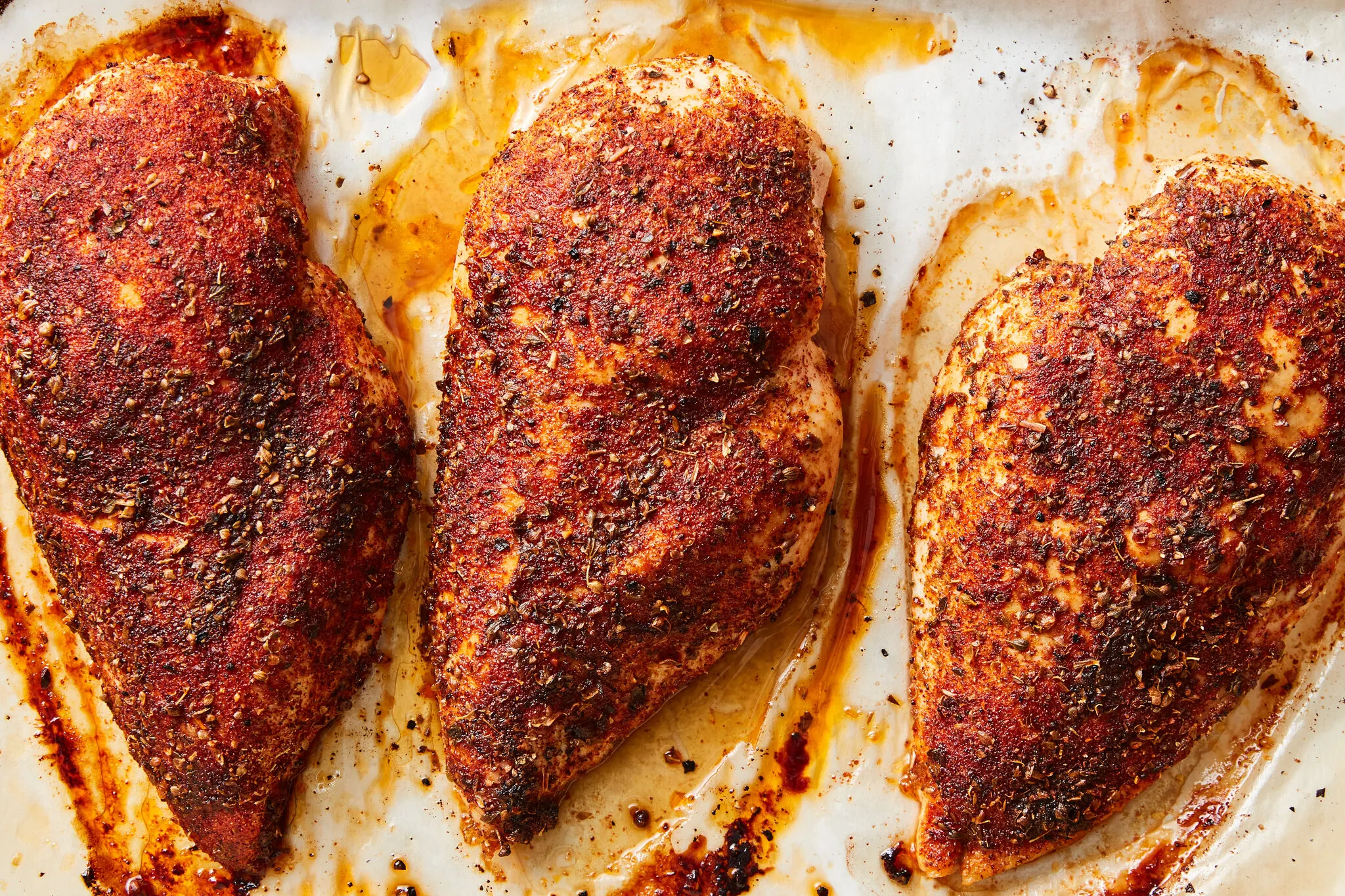 A freshly baked boneless skinless chicken breast sliced on a cutting board with visible juices, a sheet pan and roasted lemon wedges in the background