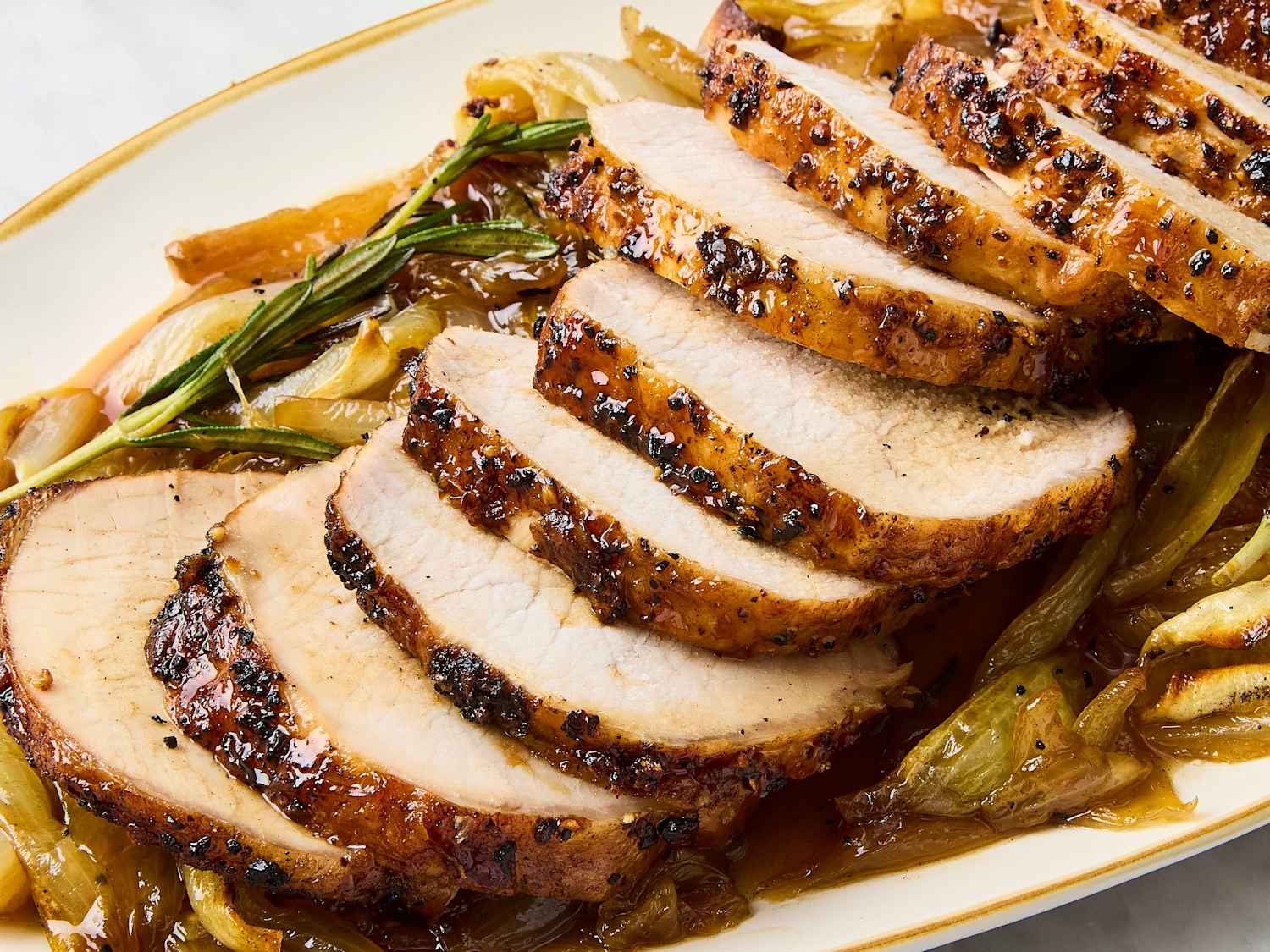 A golden-brown pork loin roast sliced into even pieces on a cutting board with visible juices and herbs
