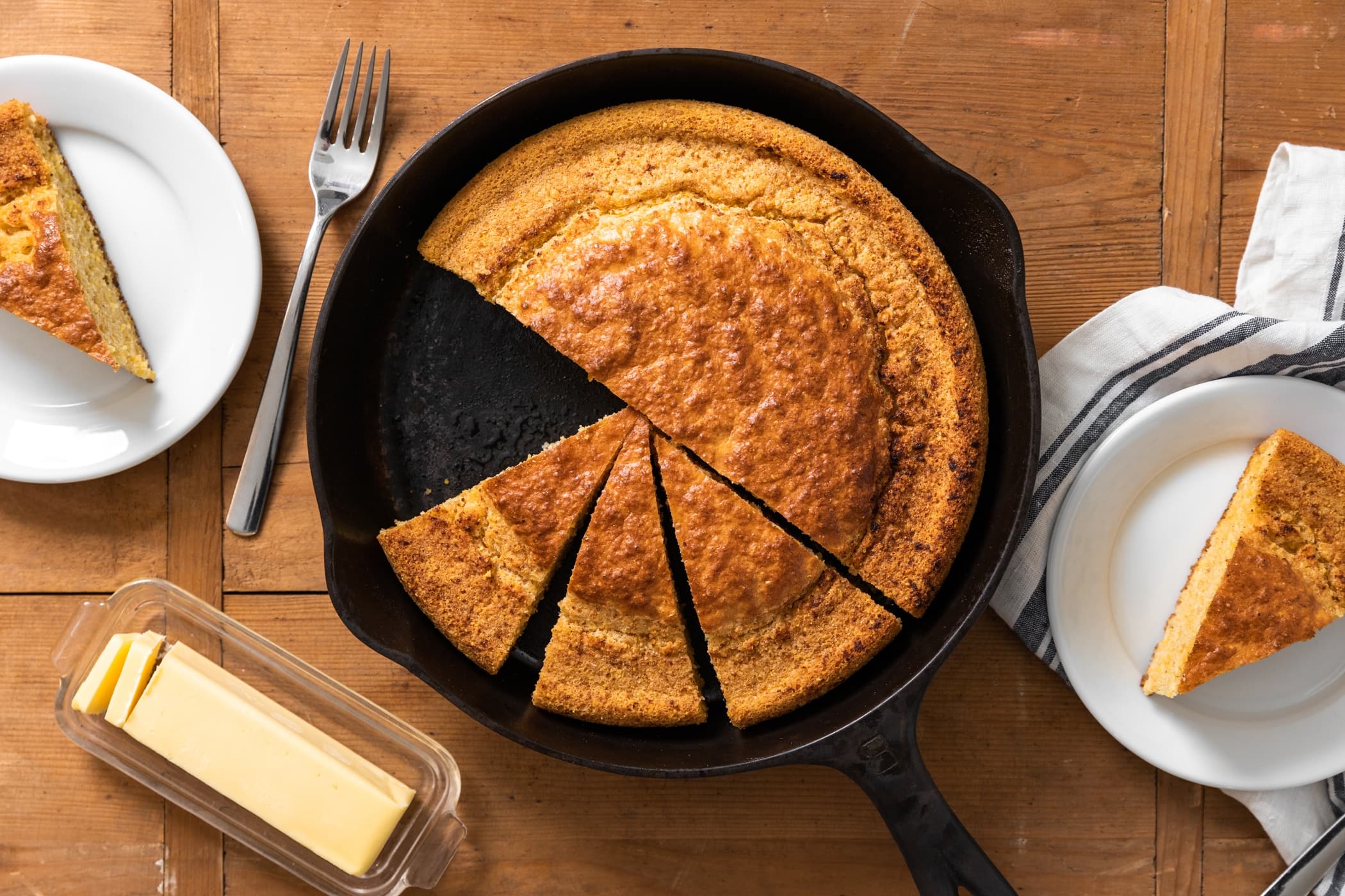 A golden cast-iron skillet cornbread with crisp, browned edges resting on a wooden cutting board in a warm home kitchen