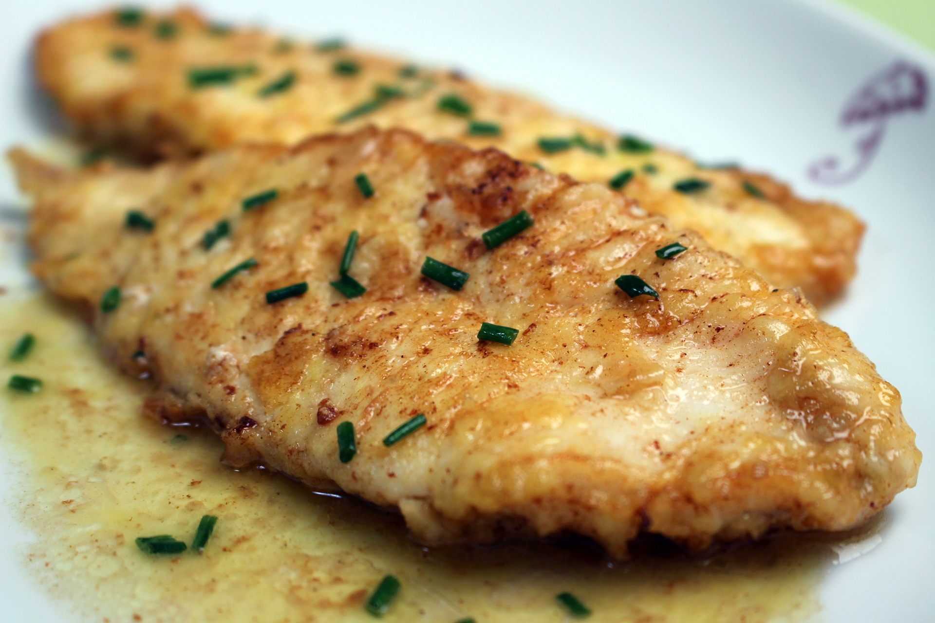 A golden pan-seared flounder fillet in a skillet with bubbling lemon-butter sauce and chopped parsley