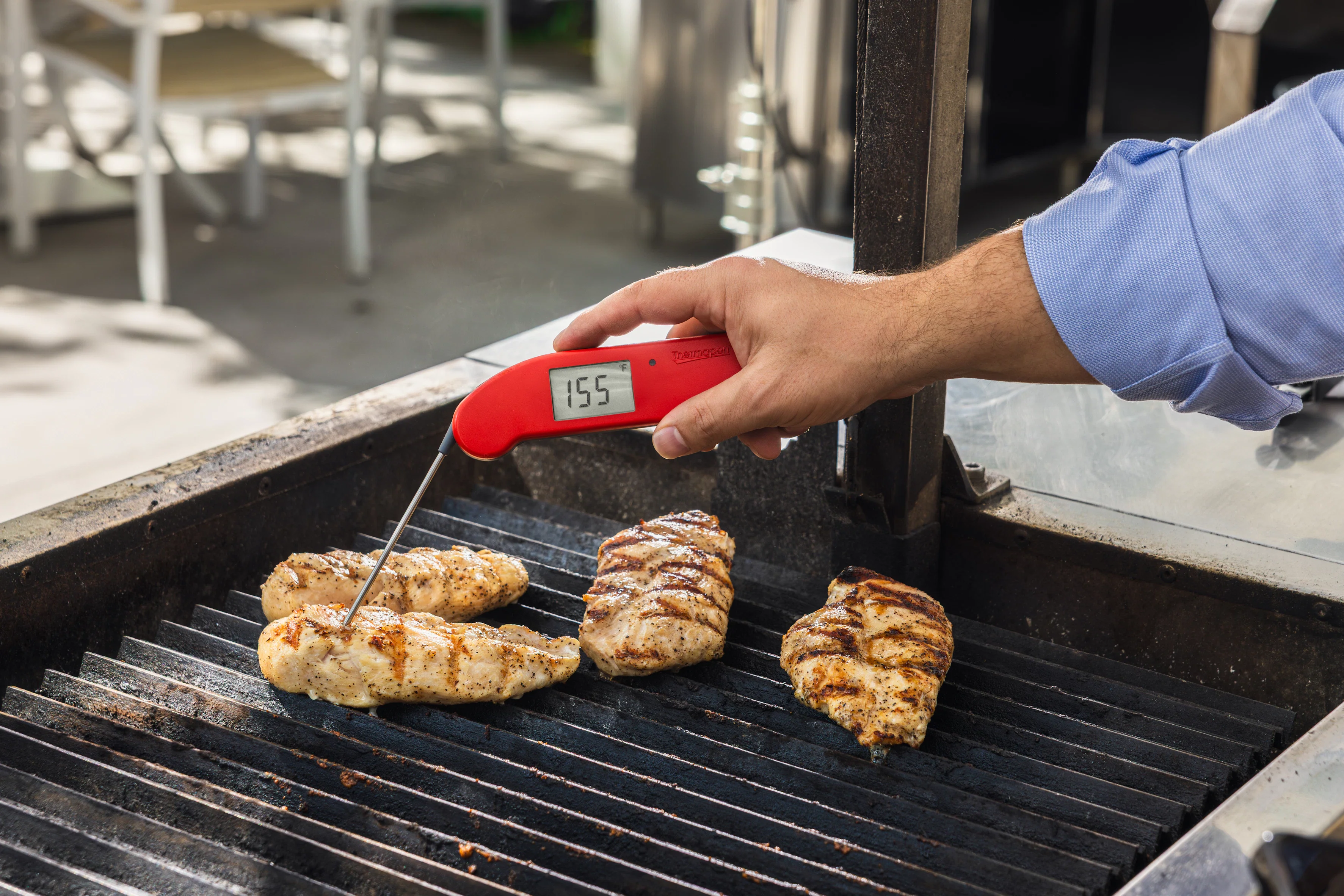A hand holding an instant-read thermometer inserted into the thickest part of a baked chicken breast on a sheet pan