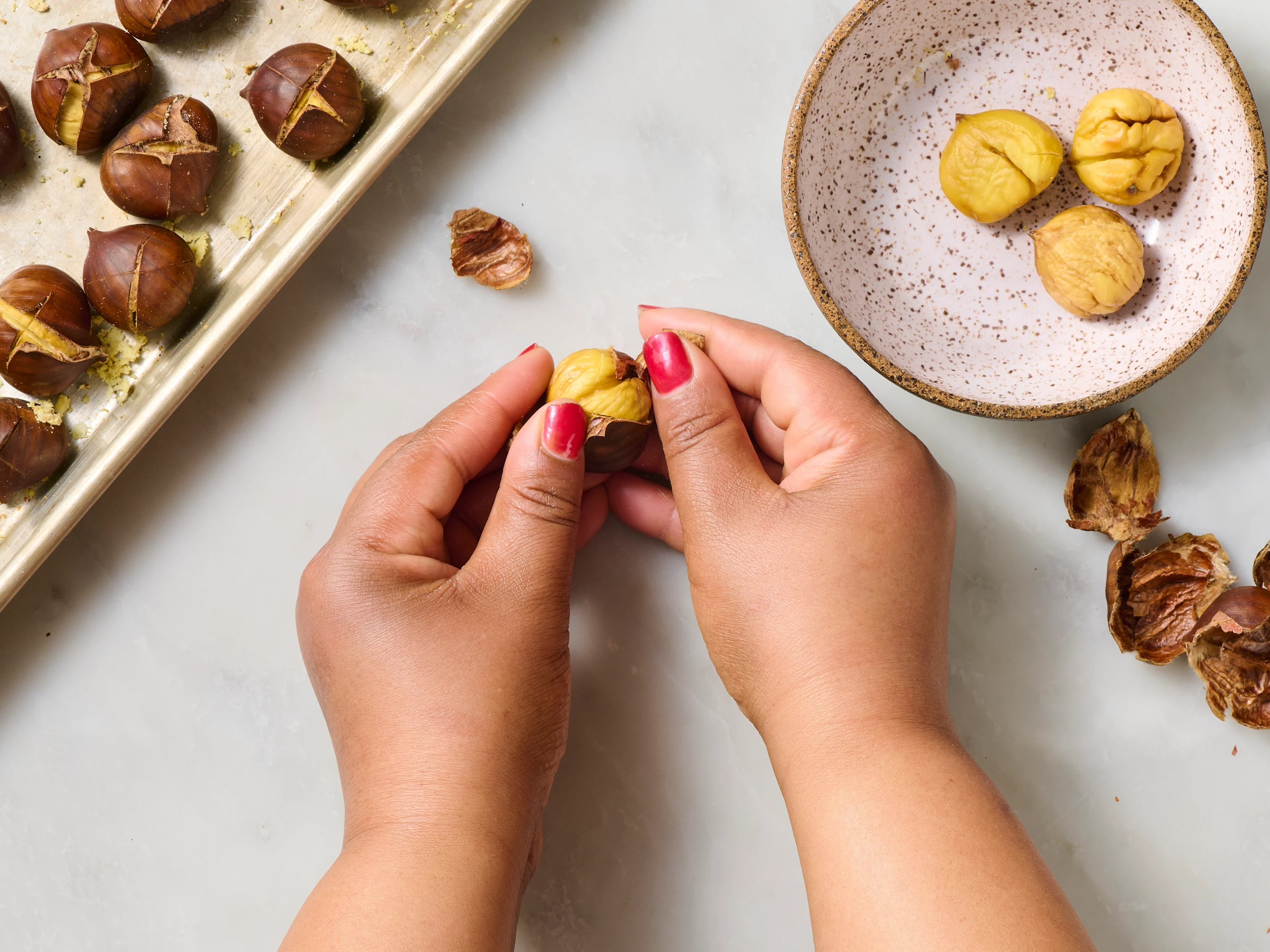 A person peeling a hot roasted chestnut, pulling back the split shell and removing the nut over a bowl