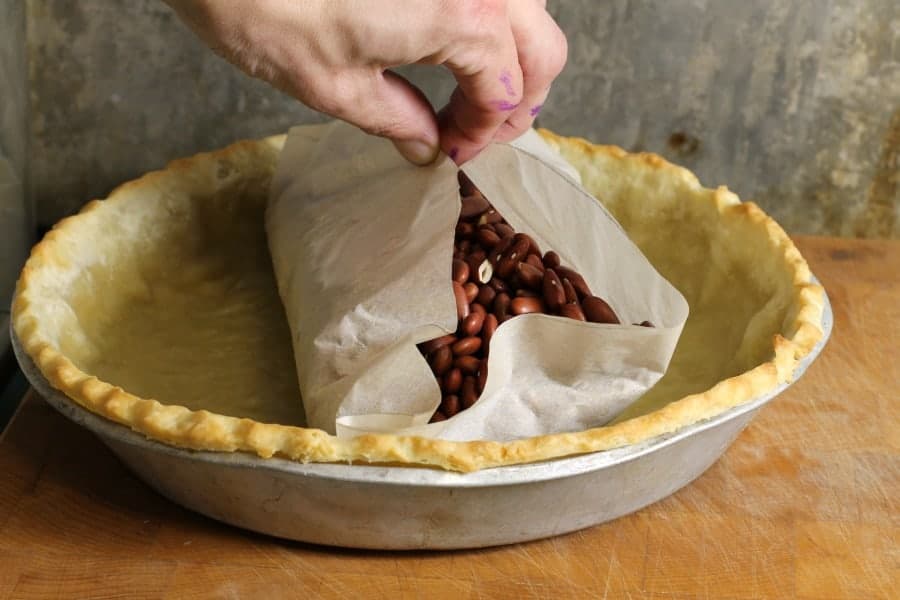 A photo of a pie shell lined with parchment paper and filled with pie weights on a baking sheet