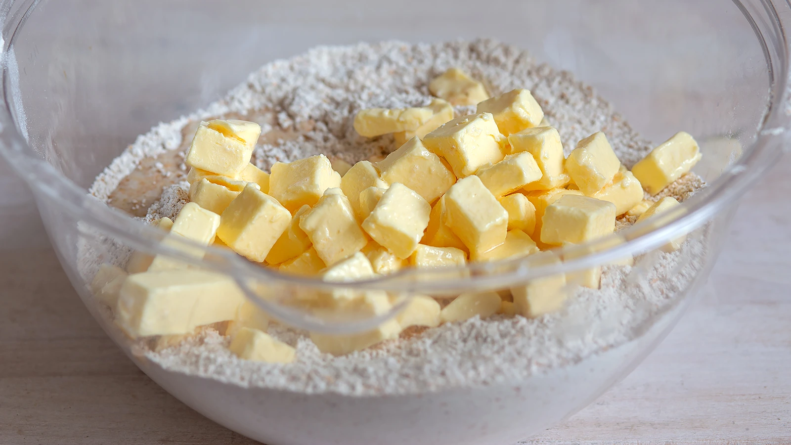 A photo of cold butter cubes scattered over flour in a mixing bowl before being cut in