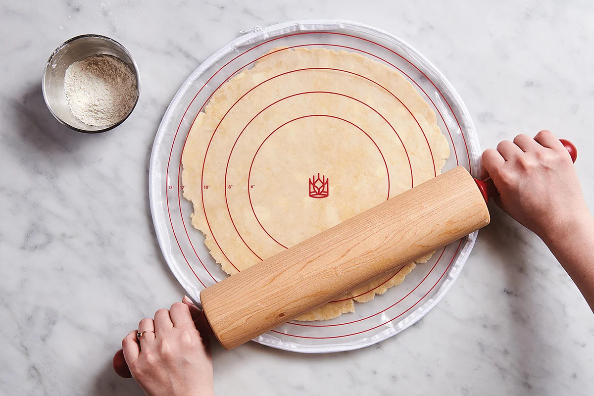A photo of hands rolling pie dough into a circle on a lightly floured countertop