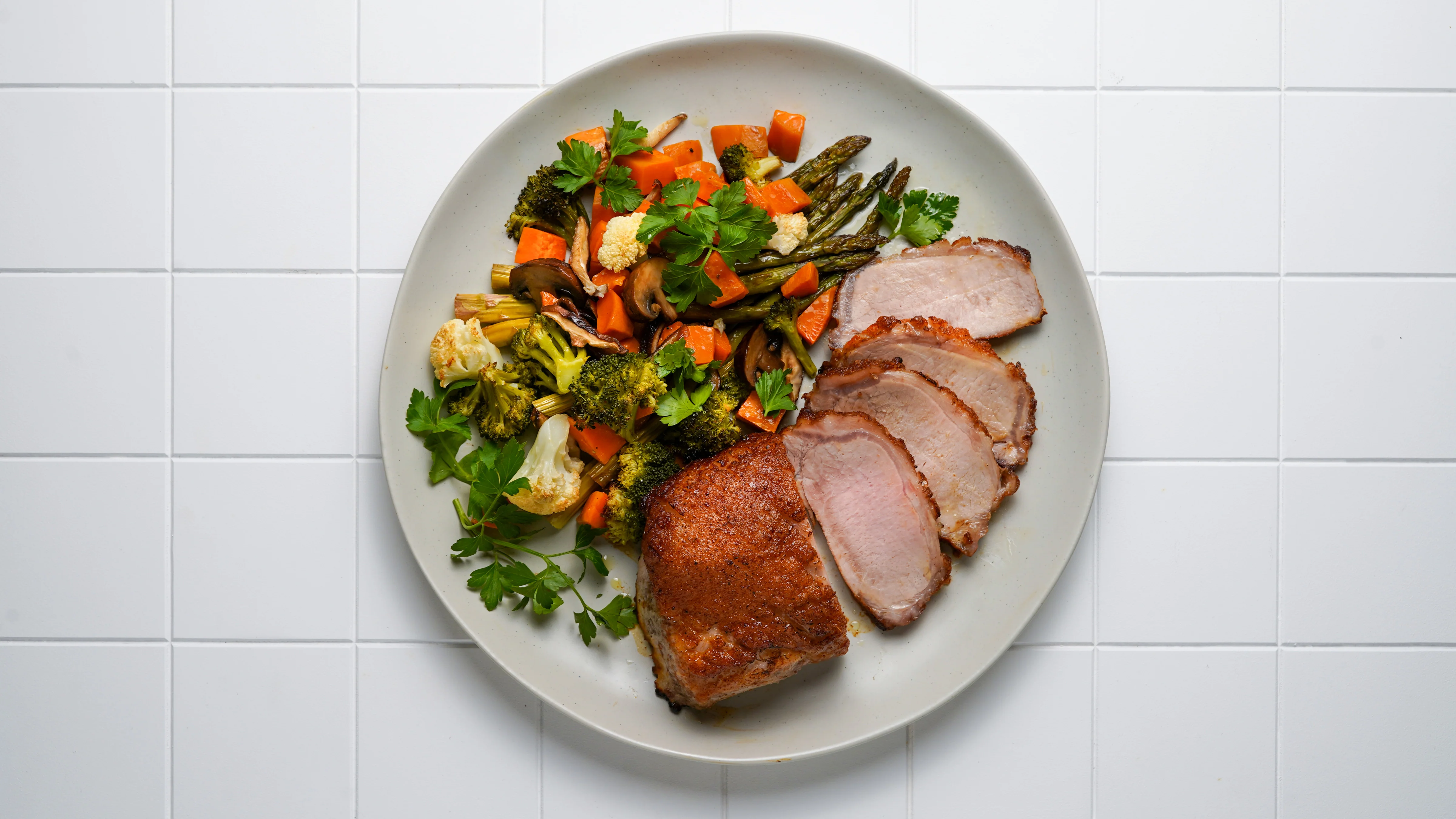 A plated pork loin roast dinner with roasted vegetables and a spoonful of pan sauce