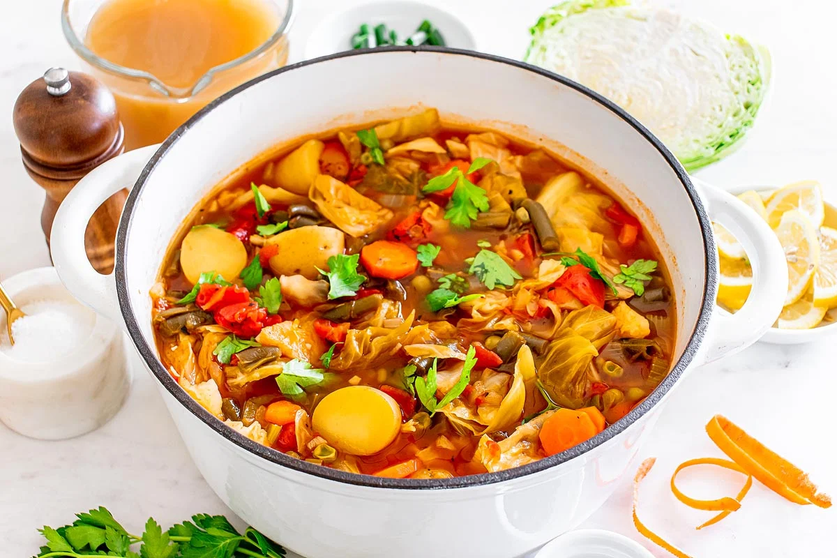 A pot of cabbage soup simmering with chopped green cabbage, carrots, celery, and herbs in a light broth