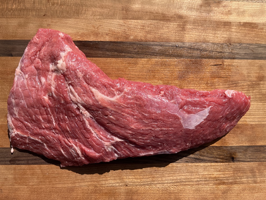 A raw triangular tri-tip roast on a rimmed sheet pan, patted dry and lightly coated with oil, showing its distinct pointed tip and wider end