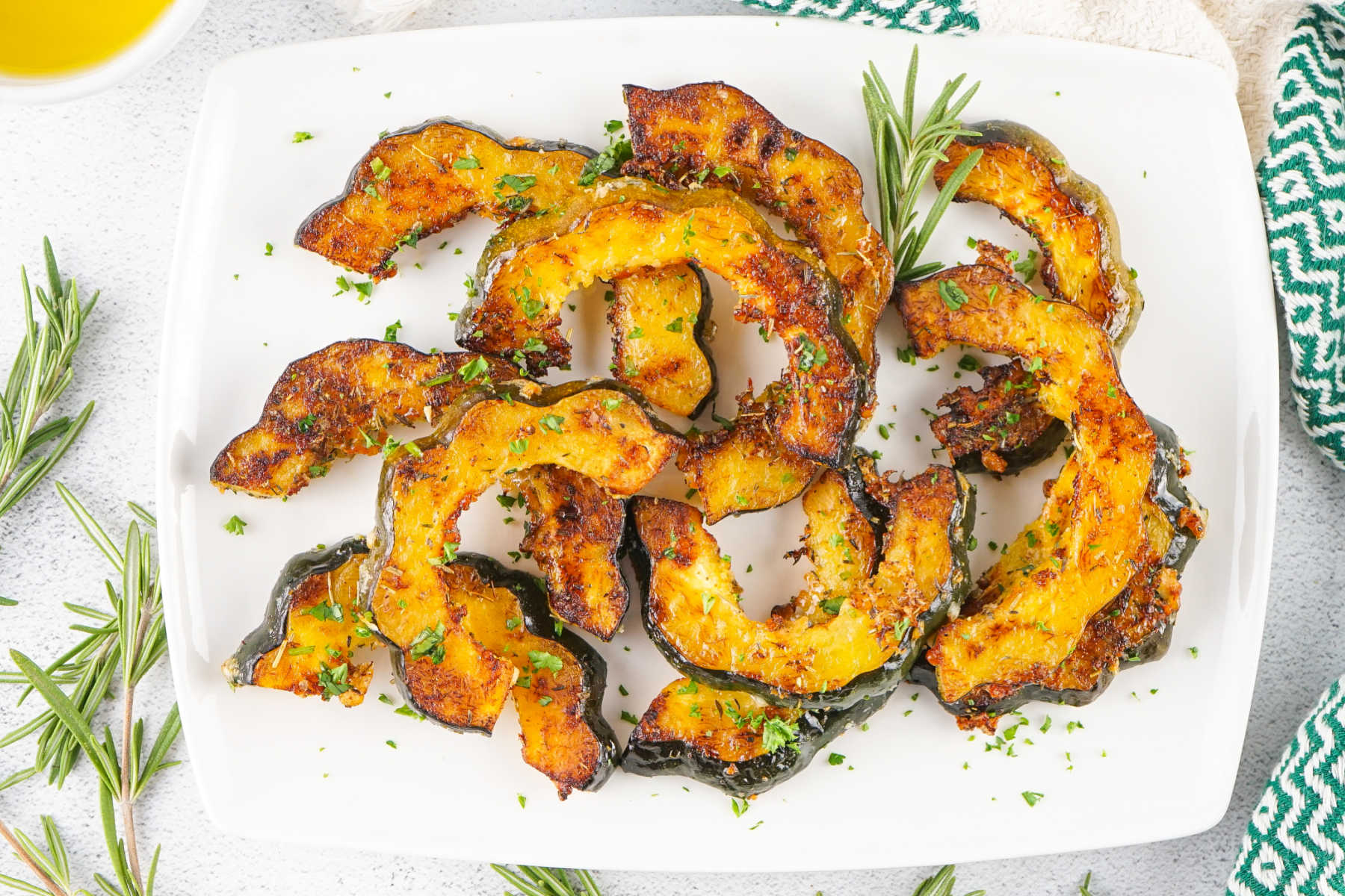 A roasted acorn squash half topped with melting garlic herb butter and scattered chopped parsley on a dinner plate
