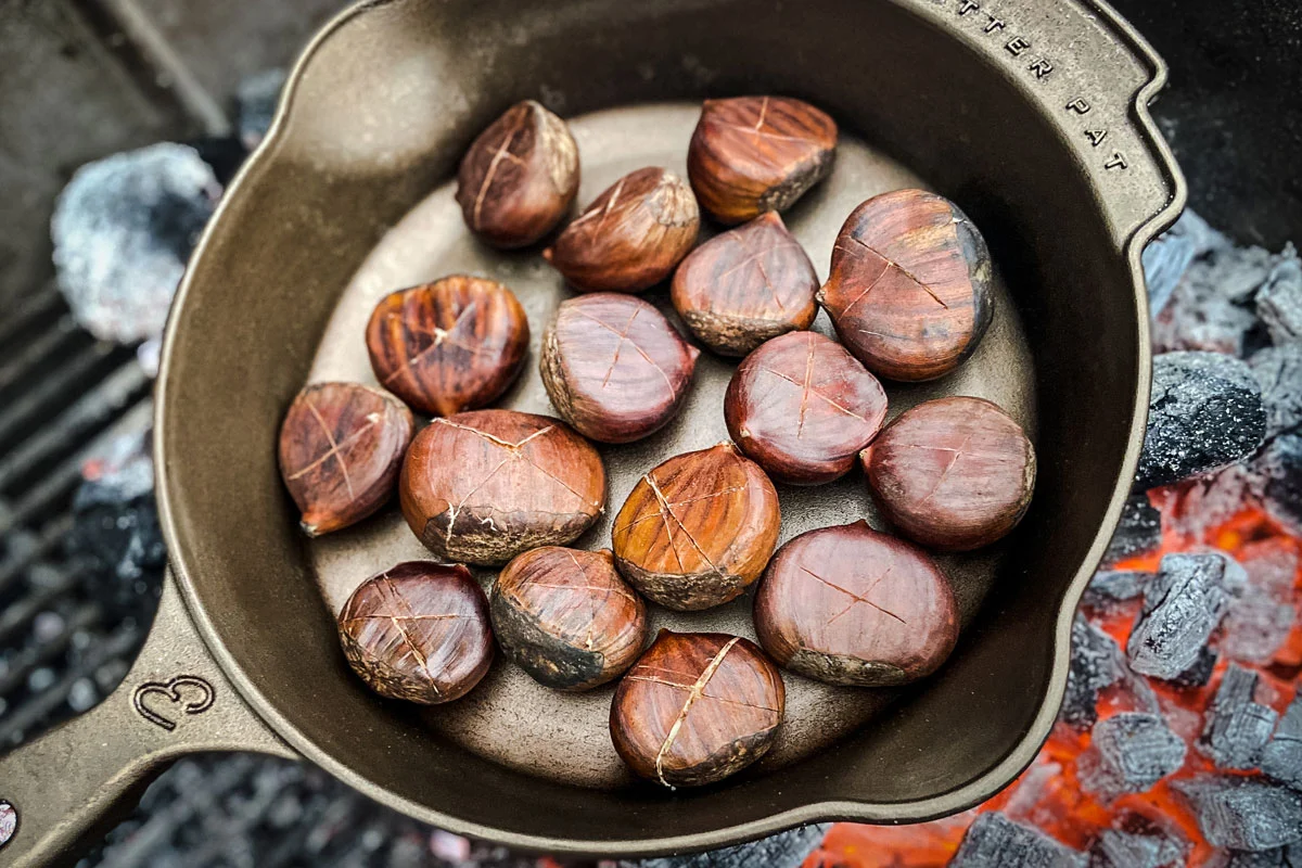 A single baking sheet of freshly roasted chestnuts with split shells, resting on a kitchen counter with a small paring knife nearby