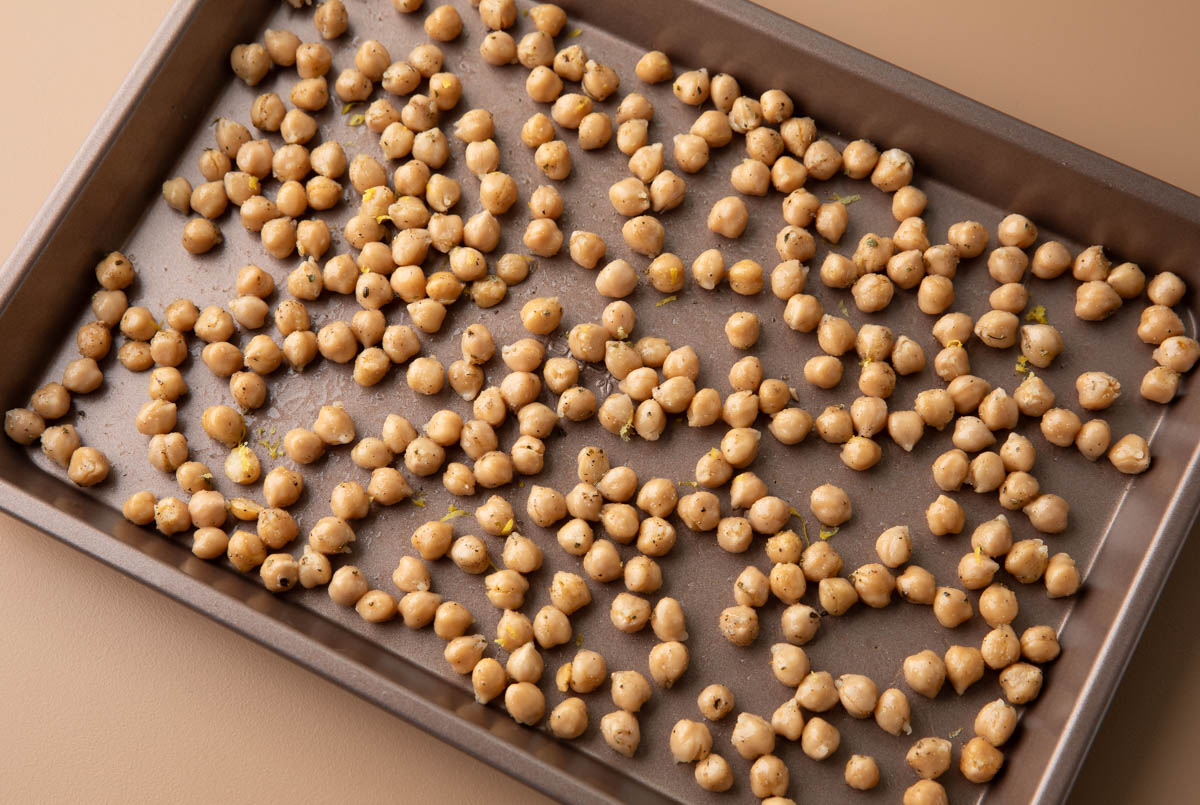 A single sheet pan filled with golden, crispy roasted chickpeas, lightly glossy from olive oil and sprinkled with salt, sitting on a kitchen counter