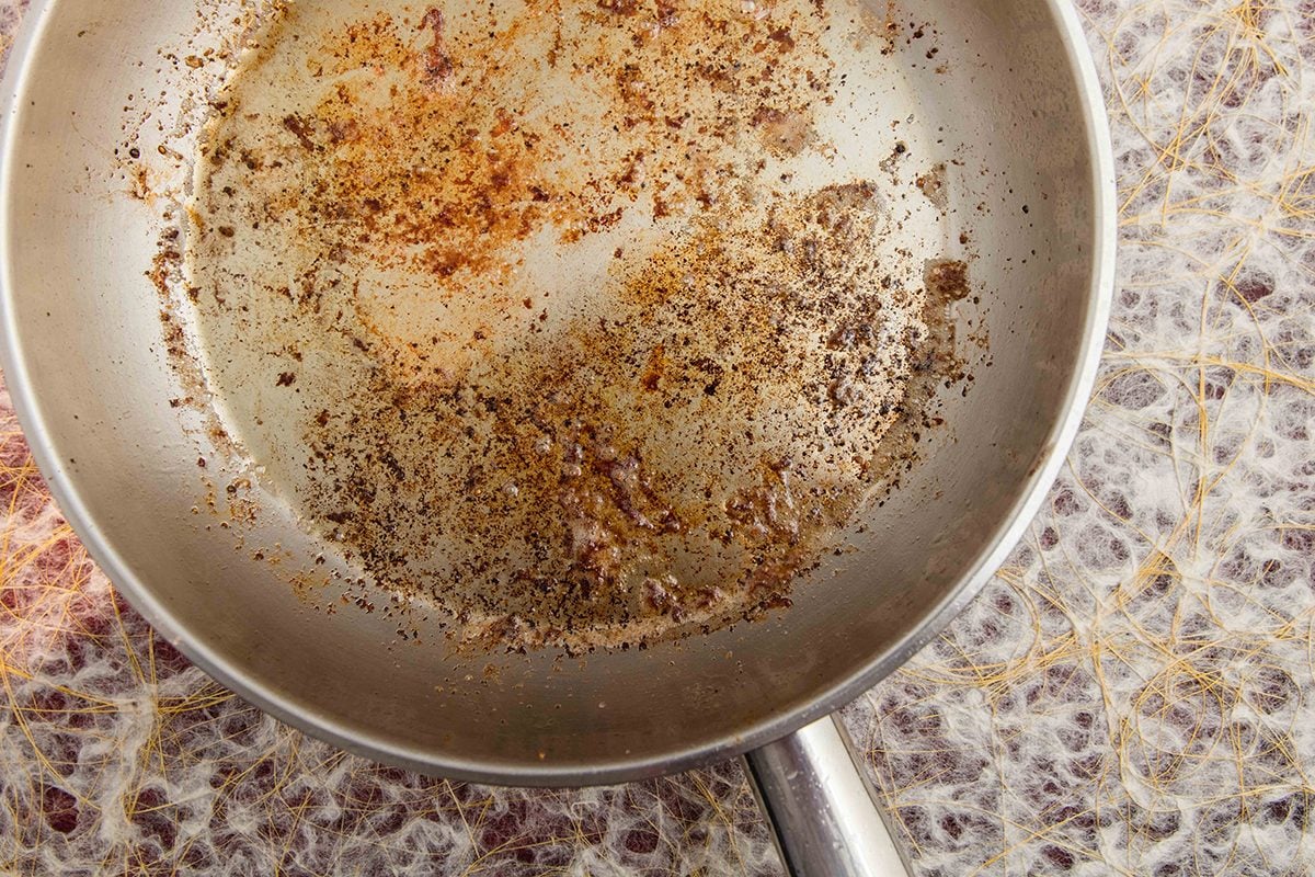 A skillet bottom with browned fond being scraped up as onions turn deep golden and glossy