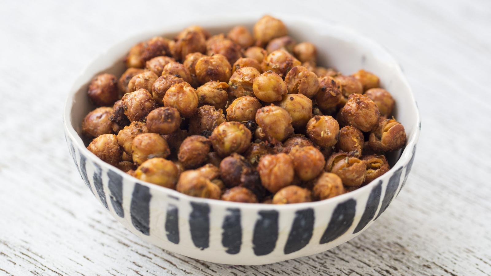 A small ceramic bowl filled with roasted chickpeas coated in warm spices, sitting on a wooden table