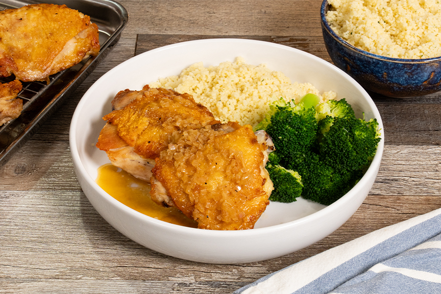 A small skillet with glossy pan sauce being whisked, with roasted chicken thighs resting on a plate in the background