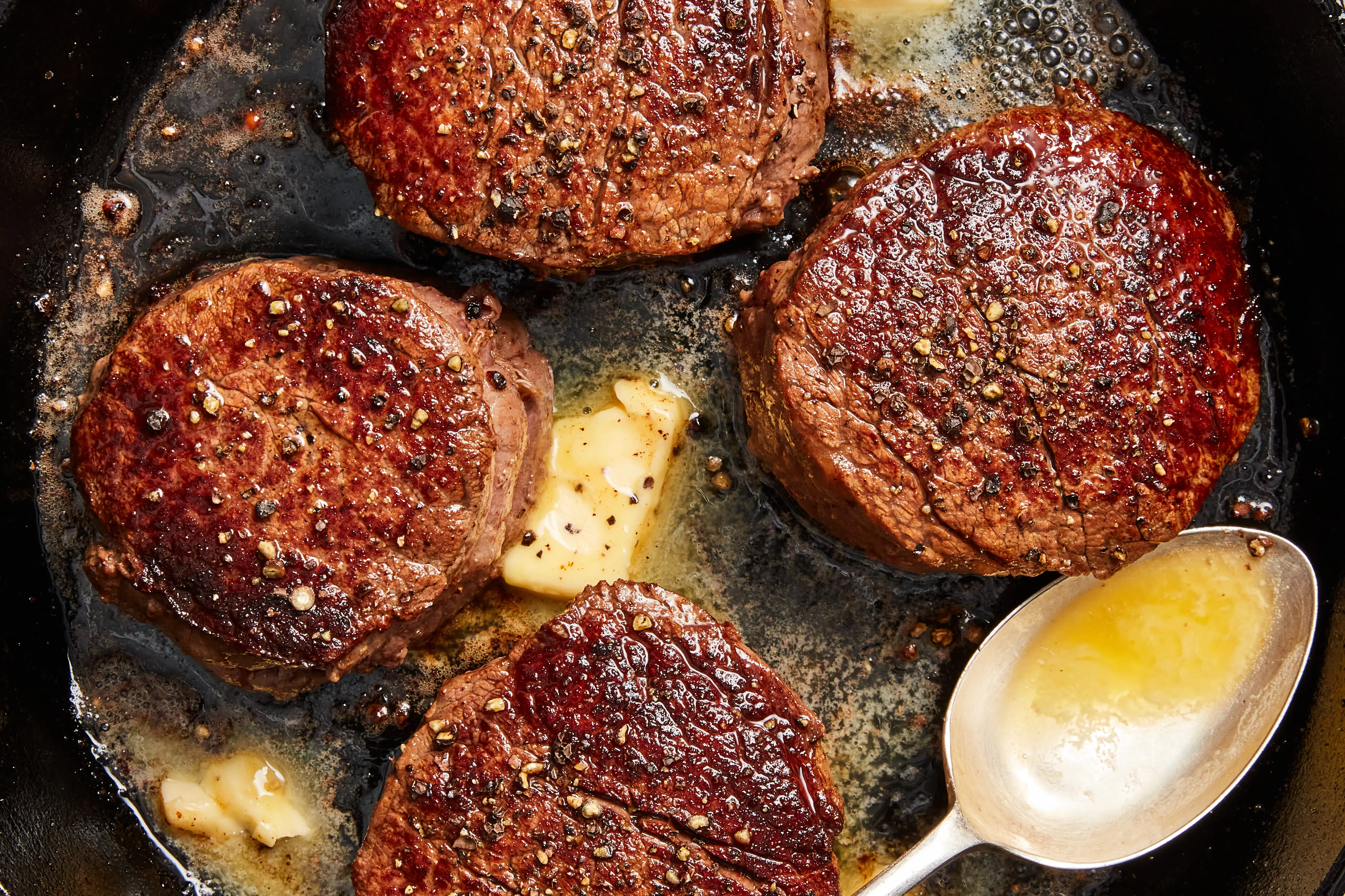 A thick filet mignon steak seared in a cast iron skillet with foaming butter, garlic cloves, and a sprig of thyme, photographed mid-baste