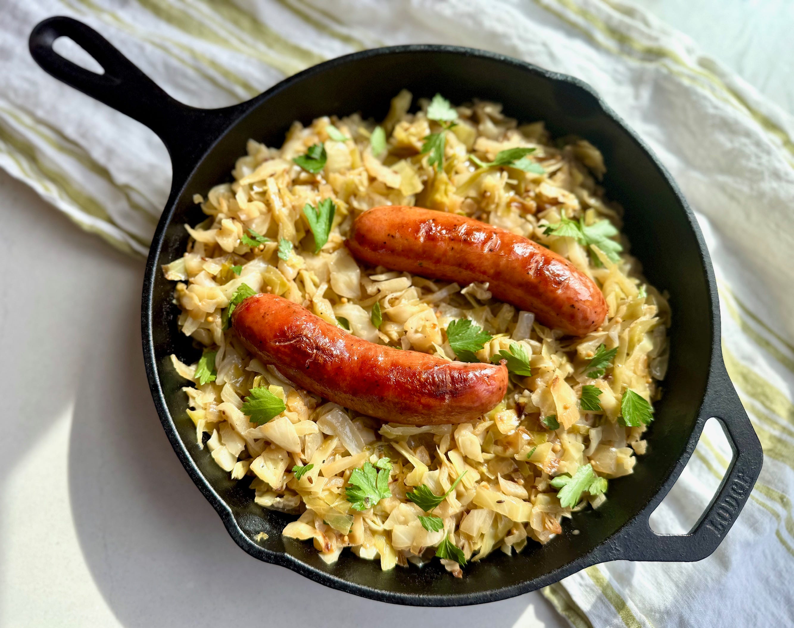 Butter-braised green cabbage ribbons glossy with melted butter in a large skillet with a wooden spoon resting on the edge
