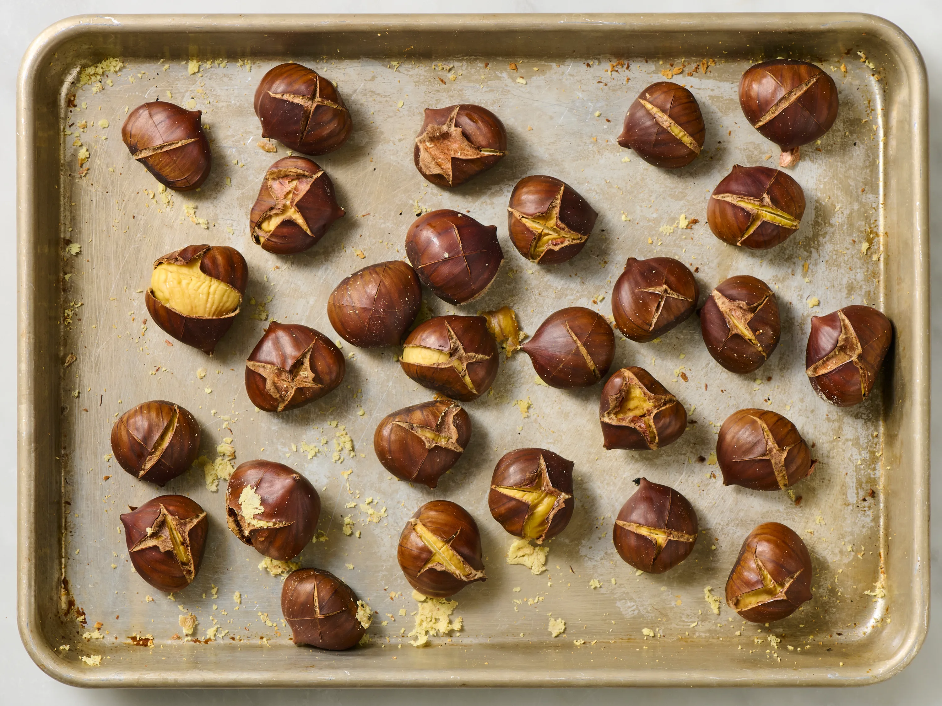Chestnuts with X scores spread in a single layer on a parchment-lined baking sheet, ready to go into the oven