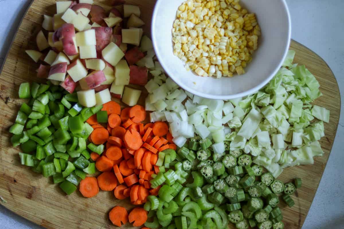 Chopped carrots, celery, onion, green beans, and potatoes arranged on a cutting board next to a chef's knife, ready for soup prep