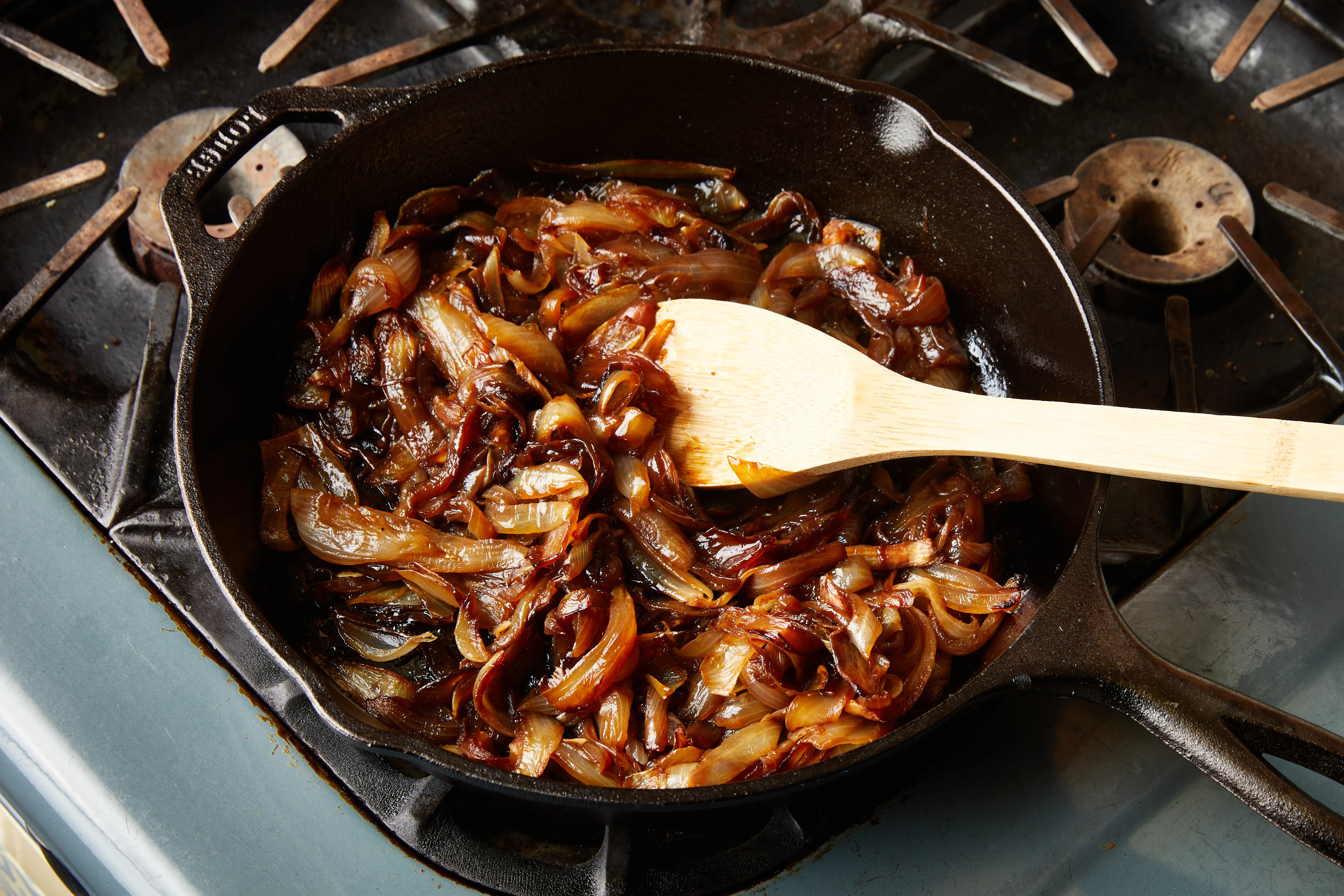 Deeply browned, jammy caramelized onions in a cast iron skillet with a wooden spoon resting on the edge in warm kitchen light
