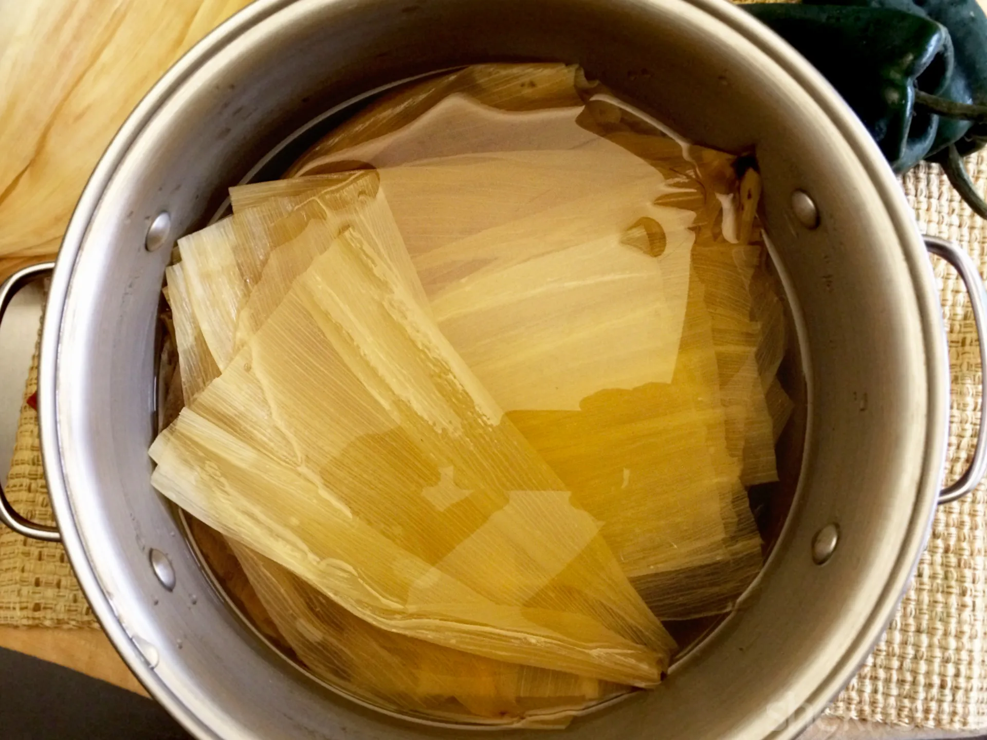 Dried corn husks soaking in a large bowl of warm water with a plate weighing them down