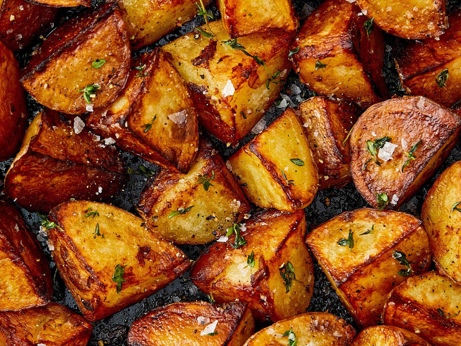 Golden-brown skillet fried potatoes with crisp edges and a tender center in a cast-iron skillet on a stovetop, with a wooden spoon nearby