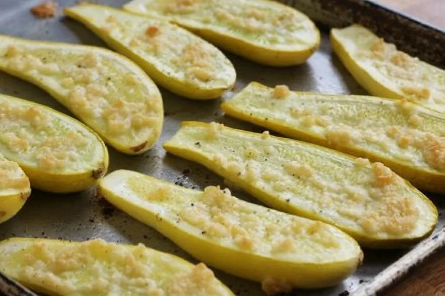 Roasted yellow squash rounds on a parchment-lined sheet pan with browned edges and scattered minced garlic