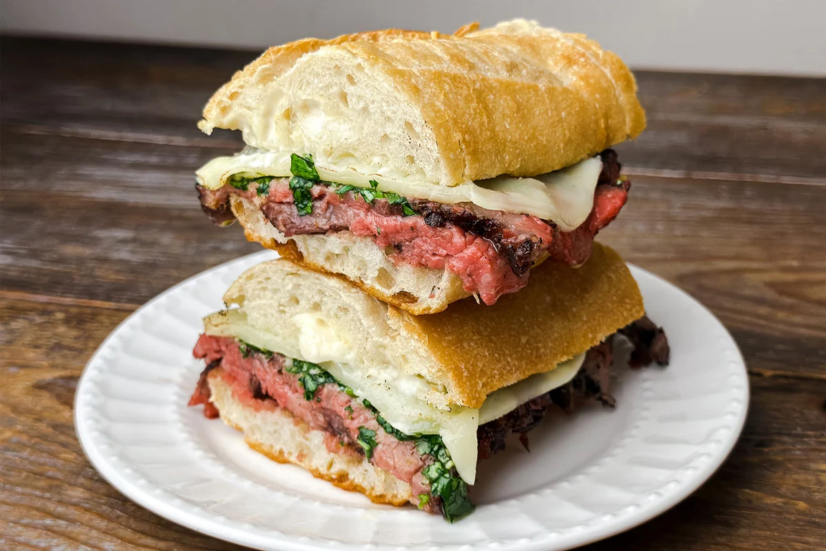 Thin slices of tri-tip piled on a toasted sandwich roll with a browned crust visible