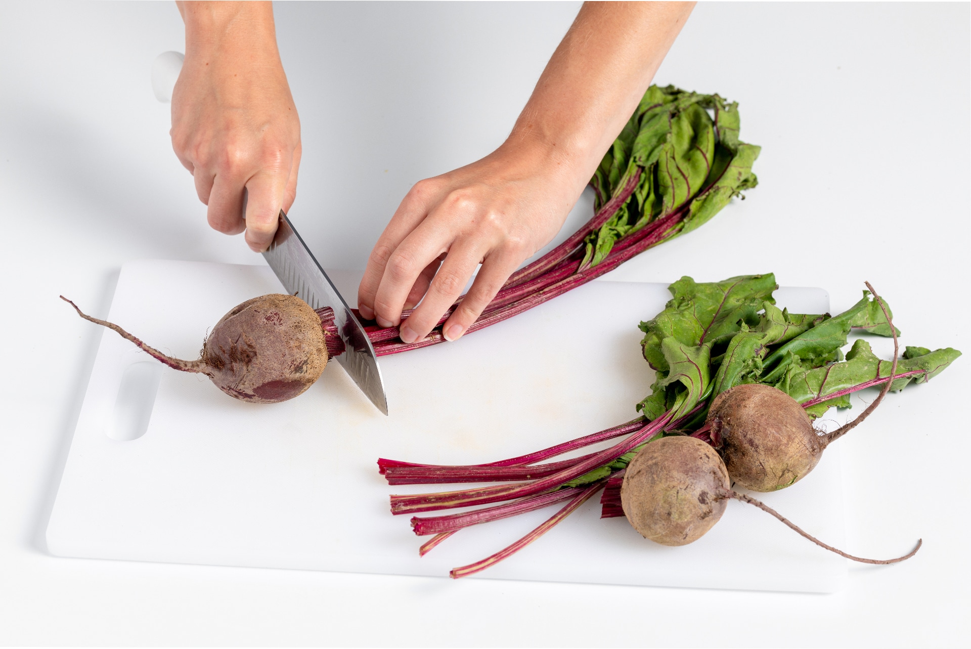 Three raw beets with the greens trimmed off, leaving short stems, sitting on a cutting board next to a vegetable brush
