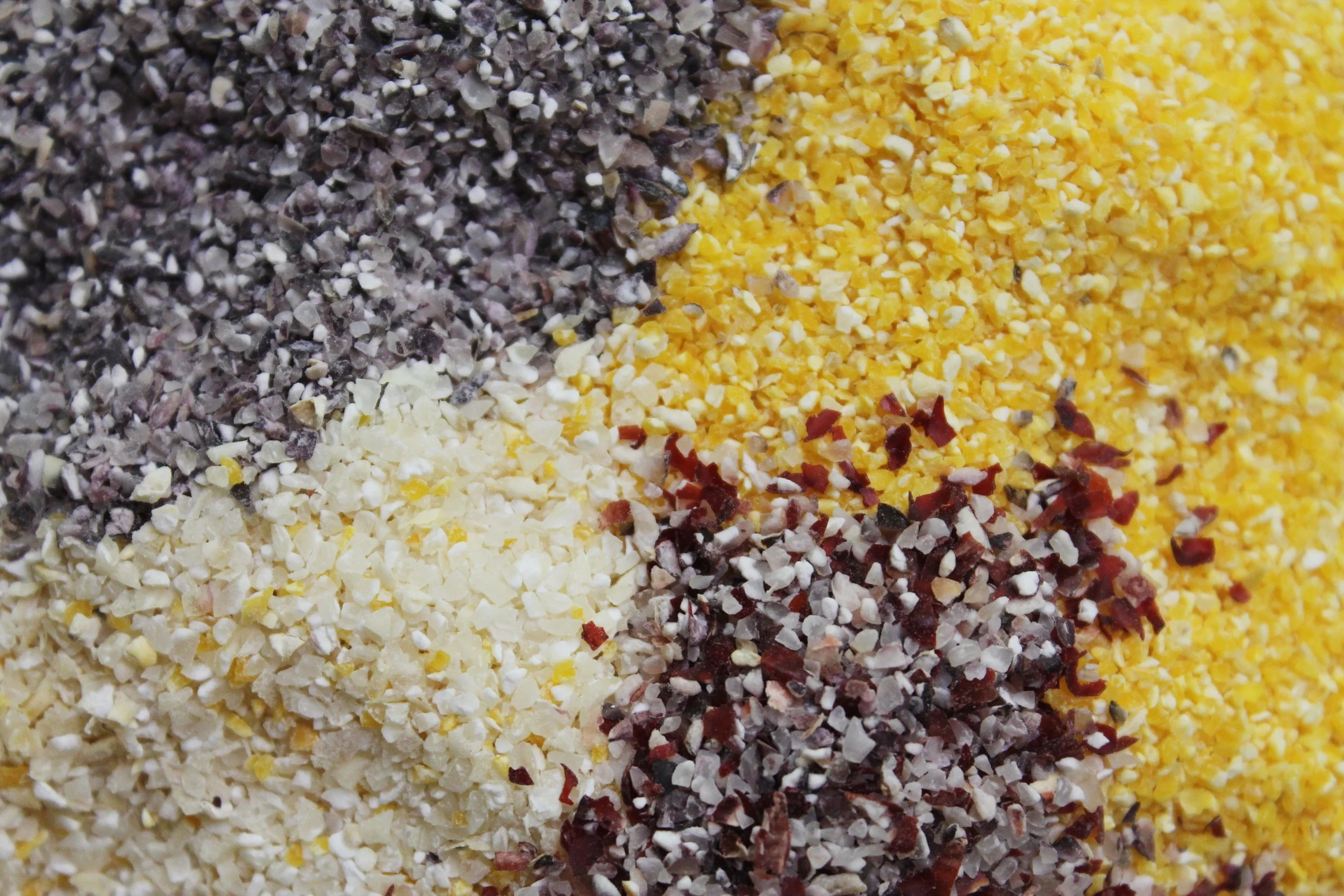 Three small bowls of cornmeal showing fine, medium, and stone-ground textures side by side on a kitchen counter