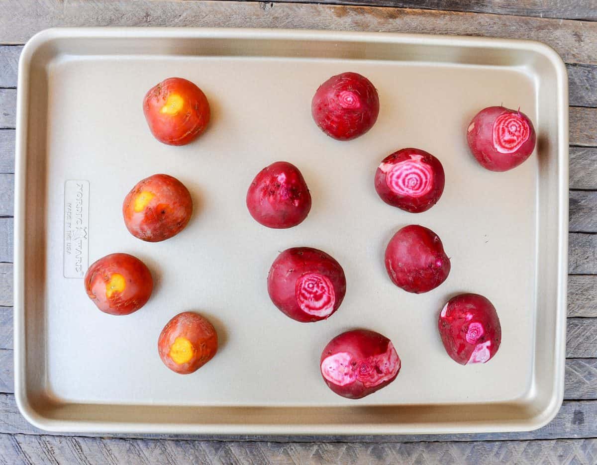 Whole roasted beets resting on a foil-lined baking sheet with a small paring knife and a clean kitchen towel nearby