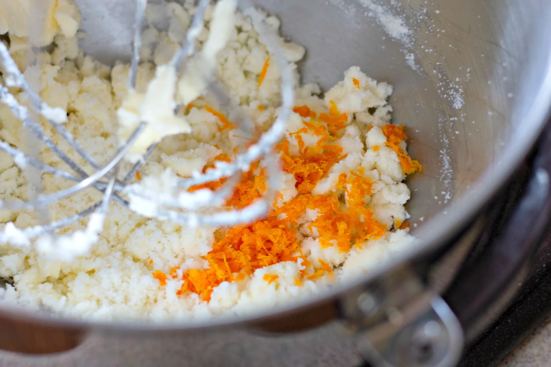 vanilla extract and orange zest being added to a mixing bowl
