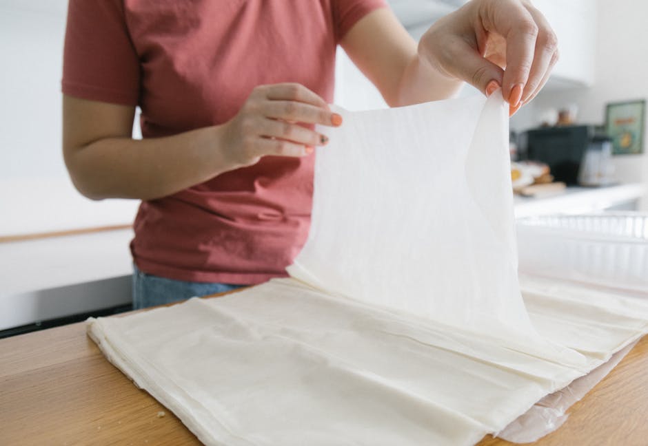 Hands demonstrating phyllo layering technique for baklava